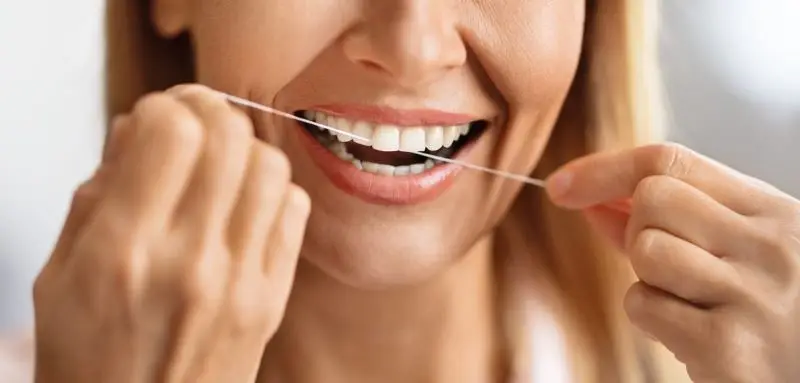 Zbliżenie uśmiechniętej kobiety używającej nić dentystyczną do czyszczenia przestrzeni międzyzębowych.